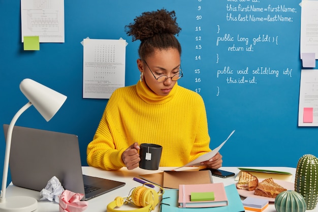 Photo gratuite expert financier femme concentré dans le contrat, examine attentivement les documents, analyse la stratégie d'entreprise, boit du thé chaud, s'assoit au bureau