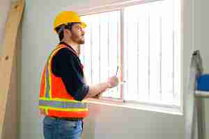 Photo gratuite expert en inspection ciblée avec un casque de sécurité vérifiant la qualité des fenêtres et des murs sur le chantier de construction