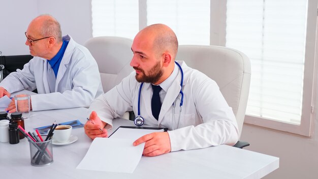 Expert médical parlant des soins de santé lors d'un séminaire avec le personnel hospitalier dans la salle de conférence pointant sur le presse-papiers. Hérapiste clinique discutant avec des collègues de la maladie, professionnel de la médecine