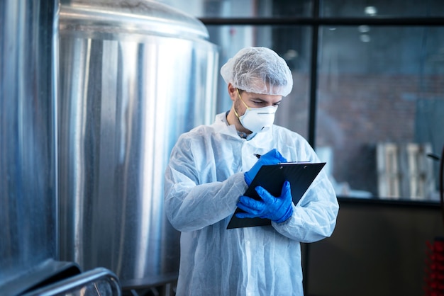 Expert technologue concentré en costume blanc contrôlant la production dans une usine alimentaire