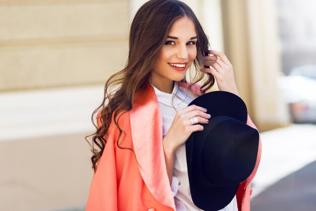 Extérieur en gros plan portrait de mode de femme décontractée élégante sexy en chapeau noir, costume rose, chemisier blanc posant sur la vieille rue. Printemps, journée ensoleillée d'automne. Coiffure ondulée.