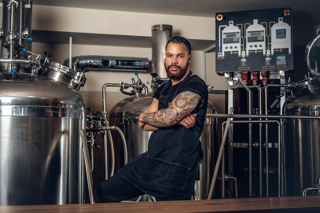 Fabricant masculin hipster tatoué à barbe noire présentant de la bière artisanale dans la microbrasserie.