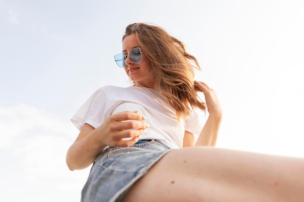 Faible angle de femme posant à l'extérieur avec des lunettes de soleil