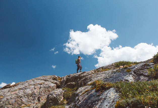 Faible angle de vue d'un homme avec un sac à dos debout au bord de la montagne sous un ciel nuageux