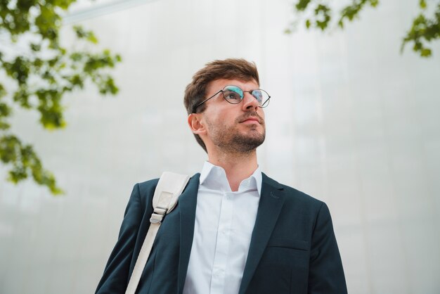 Faible angle de vue d&#39;un jeune homme d&#39;affaires debout contre le mur à la recherche de suite