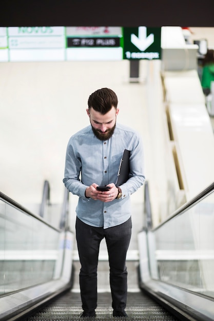 Faible angle de vue d&#39;un jeune homme d&#39;affaires permanent sur l&#39;escalator à l&#39;aide d&#39;un téléphone portable