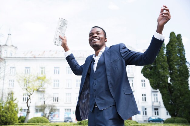 Faible angle de vue d&#39;un jeune homme d&#39;affaires sans soucis tenant le journal en levant les mains