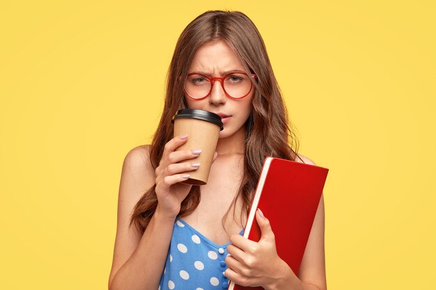 Faible esprit jeune femme avec des lunettes posant contre le mur jaune