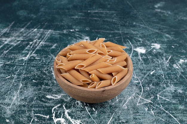 Faire dorer les pâtes penne crues dans un bol en bois. Photo de haute qualité