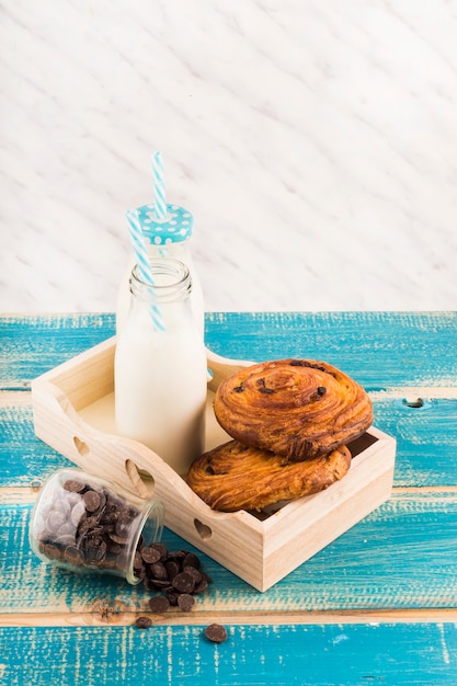 Faites tourbillonner les bouteilles de pâte et de lait dans le plateau près du pot de pépites de chocolat sur une surface en bois