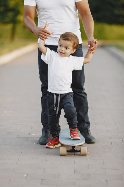 Famille asiatique dans un parc. Homme dans un t-shirt blanc. Le père apprend à son fils à faire du skate.