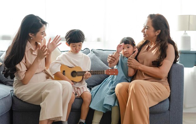 Famille asiatique heureuse avec grand-mère jouant de la guitare et chantant une chanson ensemble à la maison