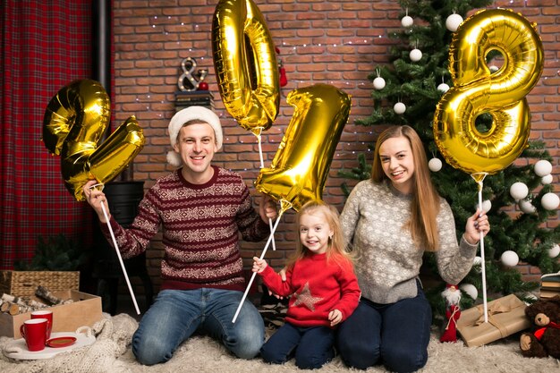 Famille assis près de l&#39;arbre de Noël tenant des ballons 2018