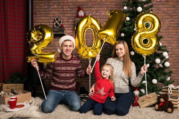 Famille assis près de l&#39;arbre de Noël tenant des ballons 2018