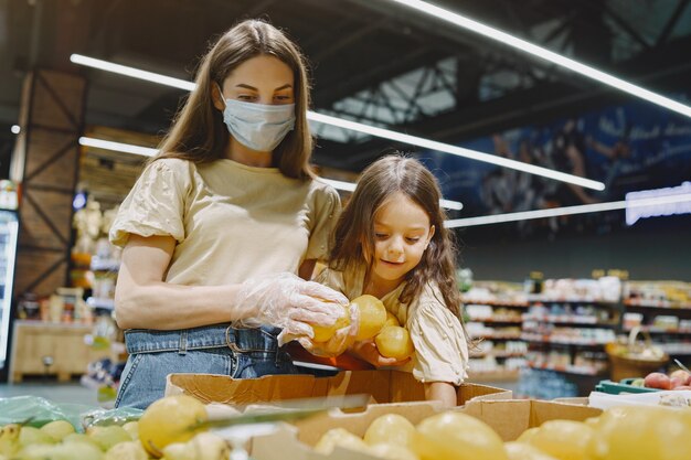 Famille au supermarché. Femme dans un masque de protection. Les gens choisissent les légumes. Mère avec fille. Coronavirus.