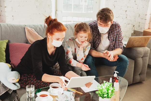 Famille caucasienne dans des masques de protection et des gants isolés à la maison