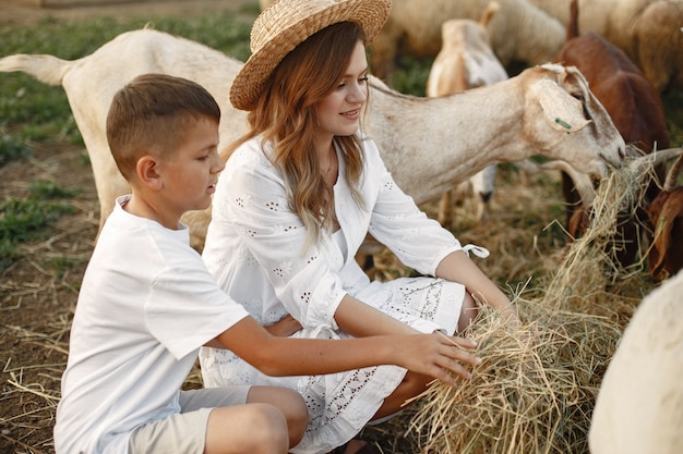 Famille dans une ferme. Les gens jouent avec des chèvres. Mère avec fils.
