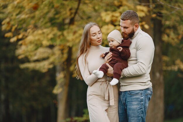 Famille dans un parc d'automne. Homme dans un pull marron. Jolie petite fille avec les parents.