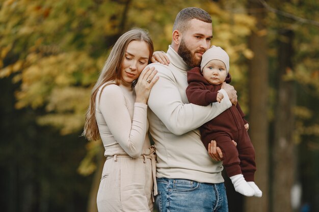 Famille dans un parc d'automne. Homme dans un pull marron. Jolie petite fille avec les parents.