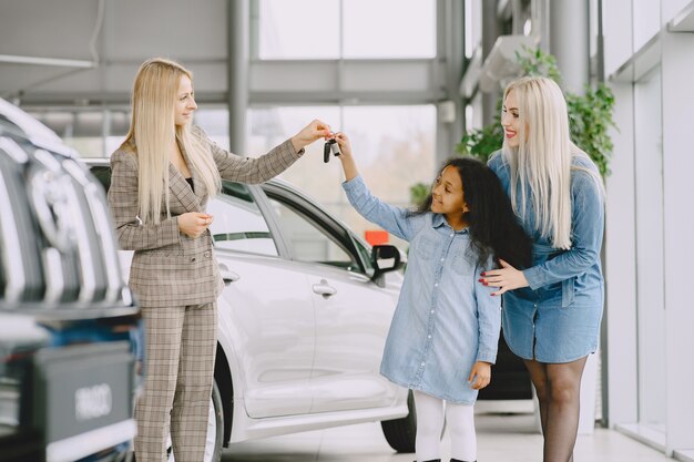 Famille dans un salon de voiture. Femme achetant la voiture. Petite fille africaine avec mther. Manager avec les clients.