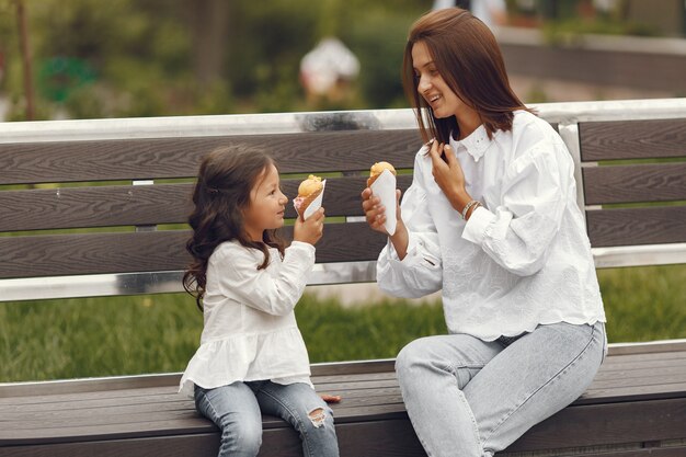 Famille dans une ville. Petite fille mange de la glace. Mère avec sa fille assise sur un banc.