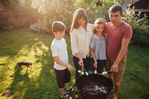 Photo gratuite famille, debout, barbecue, rôtissage, guimauve, dans parc