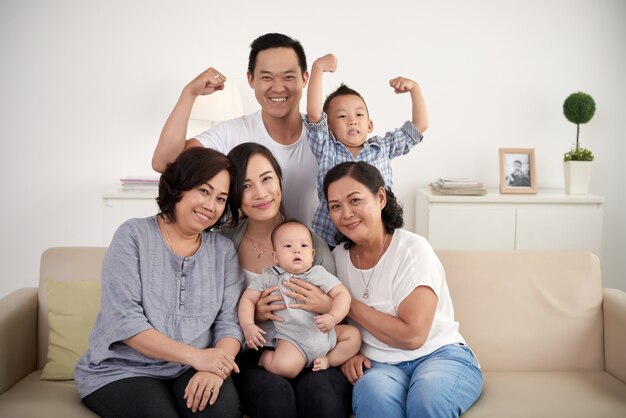 Famille élargie asiatique avec bébé et enfant en bas âge posant ensemble autour d'un canapé à la maison
