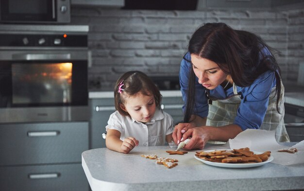 Famille heureuse dans la cuisine. Concept de nourriture de vacances. Mère et fille décorent des cookies. Famille heureuse en faisant des pâtisseries maison. Nourriture maison et petit assistant