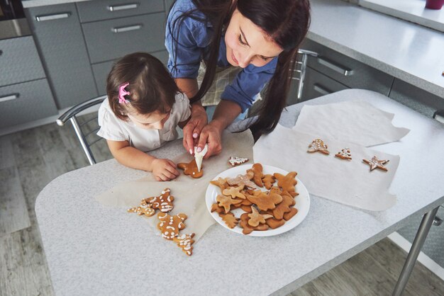 Famille heureuse dans la cuisine. Concept de nourriture de vacances. Mère et fille décorent des cookies. Famille heureuse en faisant des pâtisseries maison. Nourriture maison et petit assistant