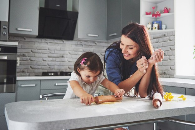 Famille heureuse dans la cuisine. Concept de nourriture de vacances. Mère et fille préparent la pâte, préparent des biscuits. Famille heureuse en faisant des cookies à la maison. Nourriture maison et petit assistant