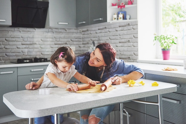 Famille heureuse dans la cuisine. Concept de nourriture de vacances. Mère et fille préparent la pâte, préparent des biscuits. Famille heureuse en faisant des cookies à la maison. Nourriture maison et petit assistant