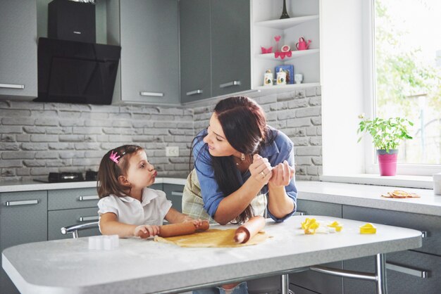 Famille heureuse dans la cuisine. Concept de nourriture de vacances. Mère et fille préparent la pâte, préparent des biscuits. Famille heureuse en faisant des cookies à la maison. Nourriture maison et petit assistant