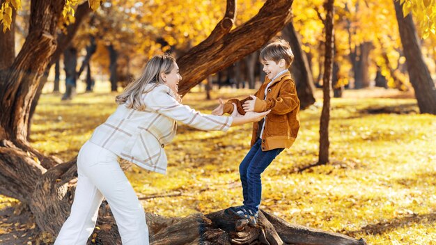 Famille heureuse dans un parc d'automne Mère jouant avec son fils sur un tronc d'arbre arbres jaunis autour