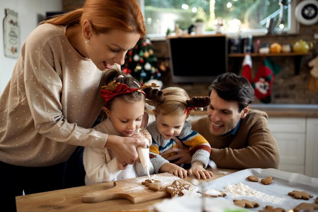 Famille heureuse décorant des biscuits de pain d'épice tout en se préparant pour les vacances de Noël