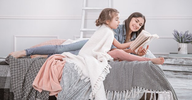 Famille heureuse. Mère et fille lisant un livre sur le lit.