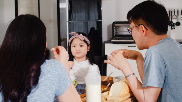 Famille japonaise asiatique prend le petit déjeuner à la maison. Maman, papa et fille asiatiques se sentant heureux de parler ensemble tout en mangeant du pain, des céréales de flocons de maïs et du lait dans un bol sur la table dans la cuisine le matin.