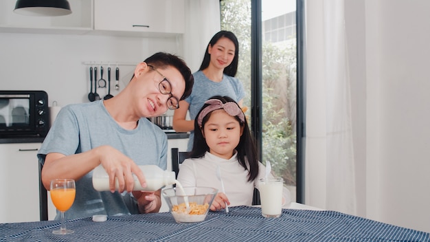 Famille japonaise asiatique prend le petit déjeuner à la maison. Maman, papa et fille asiatiques se sentant heureux de parler ensemble tout en mangeant du pain, des céréales de flocons de maïs et du lait dans un bol sur la table dans la cuisine le matin.