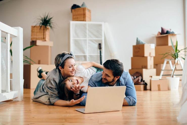 Photo gratuit famille joyeuse utilisant un ordinateur portable tout en se relaxant sur le sol de leur nouvelle maison