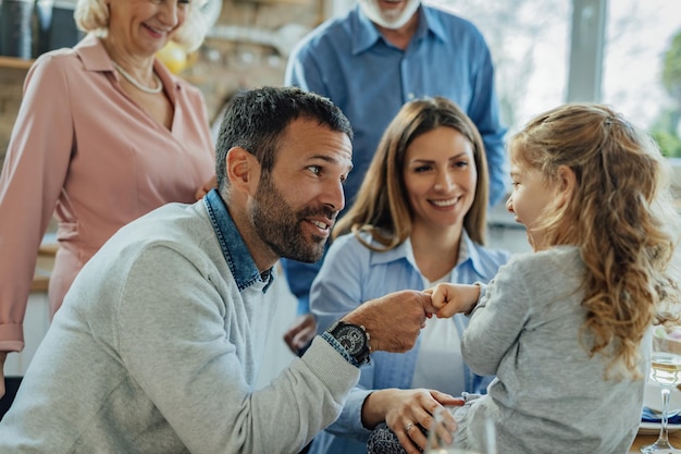 Famille multigénérationnelle profitant du temps ensemble à la maison. L'accent est mis sur un père heureux qui parle à sa petite fille et passe un accord avec elle.