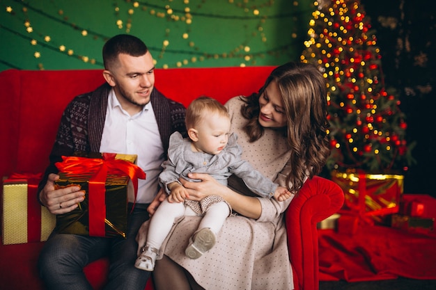 Famille à Noël assis sur un canapé rouge par l&#39;arbre de Noël