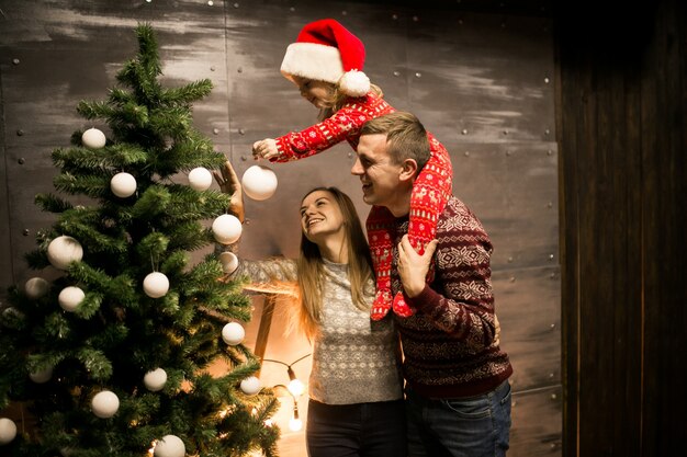 Famille par le sapin de Noël avec petite fille au chapeau rouge