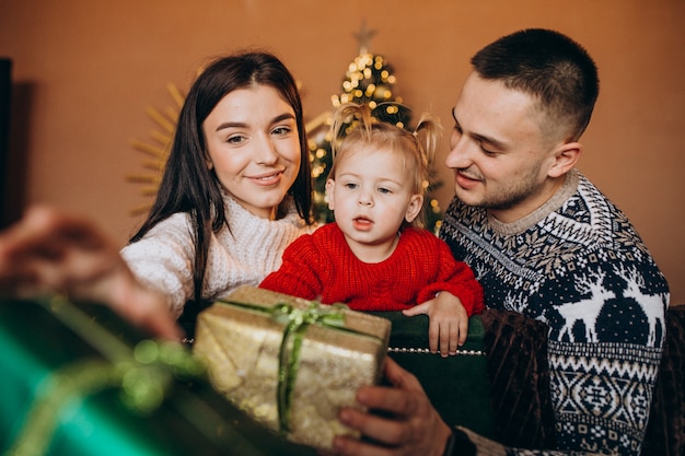 Famille avec petite fille assise devant un arbre de Noël et une boîte-cadeau déballée