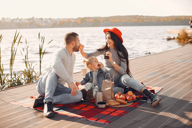 Famille avec petite fille assise près de l'eau dans un parc en automne