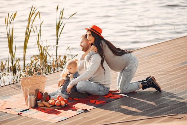 Famille avec petite fille assise près de l'eau dans un parc en automne