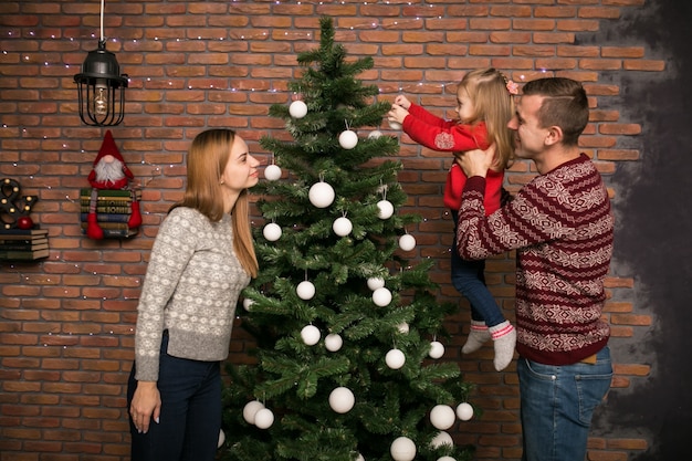 Famille avec petite fille suspendue des jouets sur un arbre de Noël