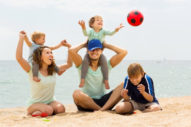 Famille positive de cinq jouant à la plage de la mer