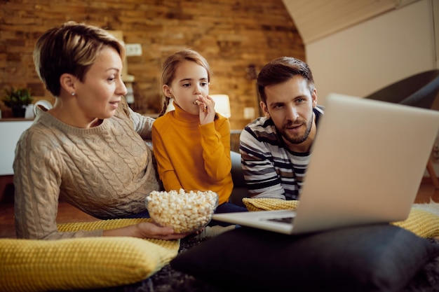 Famille utilisant un ordinateur portable tout en mangeant du pop-corn et en se relaxant à la maison