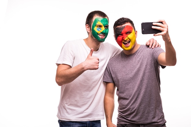 Les fans de football supporters avec visage peint des équipes nationales du Brésil et de l'Allemagne prennent selfie isolé sur fond blanc