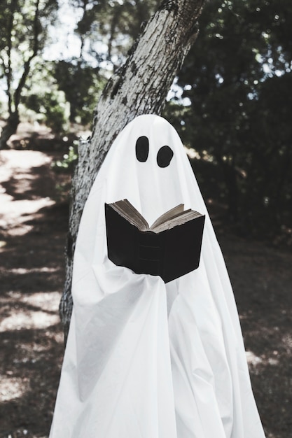 Photo gratuite fantôme appuyé sur un arbre et livre de lecture