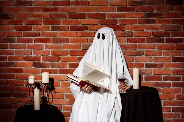 Photo gratuite fantôme tenant le livre et le vin sur le mur de briques. fête d'halloween.